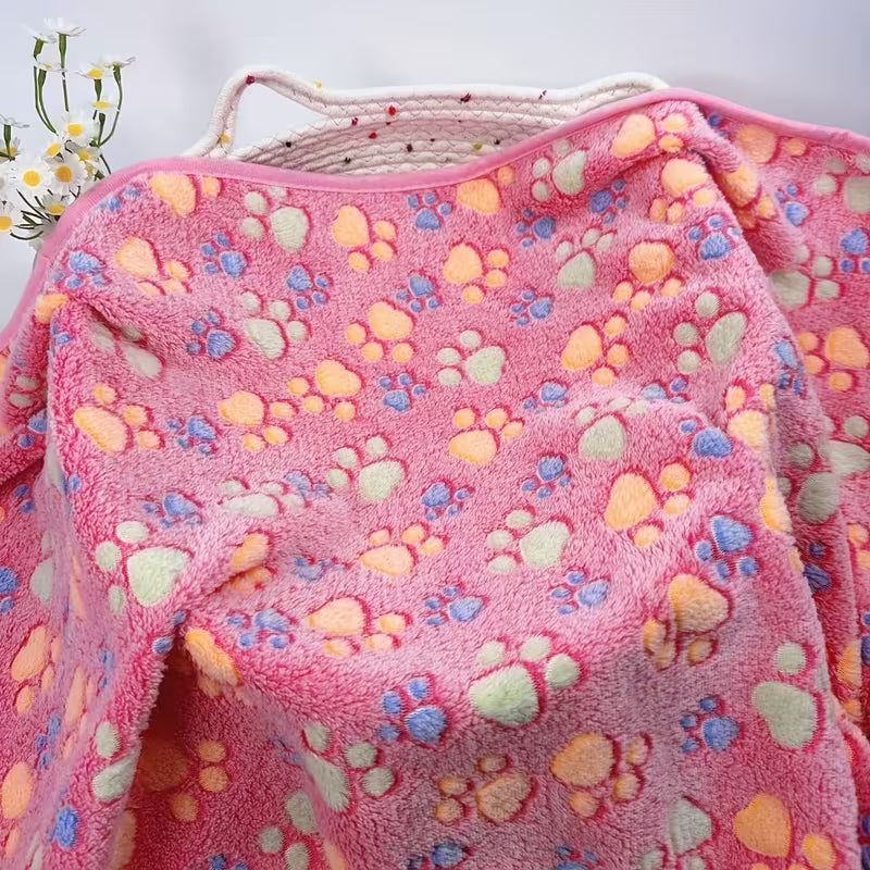 Pink pet blanket with colourful paw prints draped over a white surface.