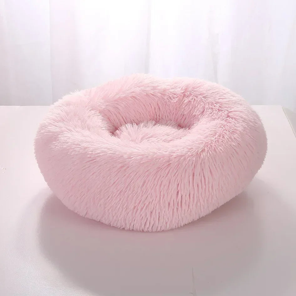 Pink fluffy donut pet bed on a white surface with a light background