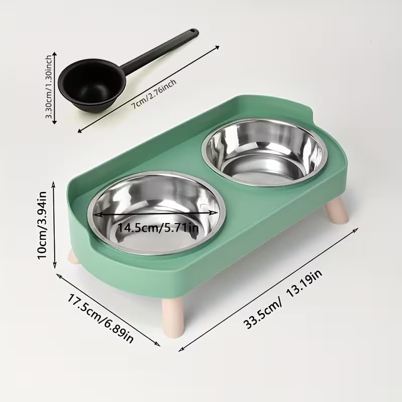 A green elevated pet feeder with two stainless steel bowls and small legs, shown with dimension callouts and a small black scoop on a light grey background.
