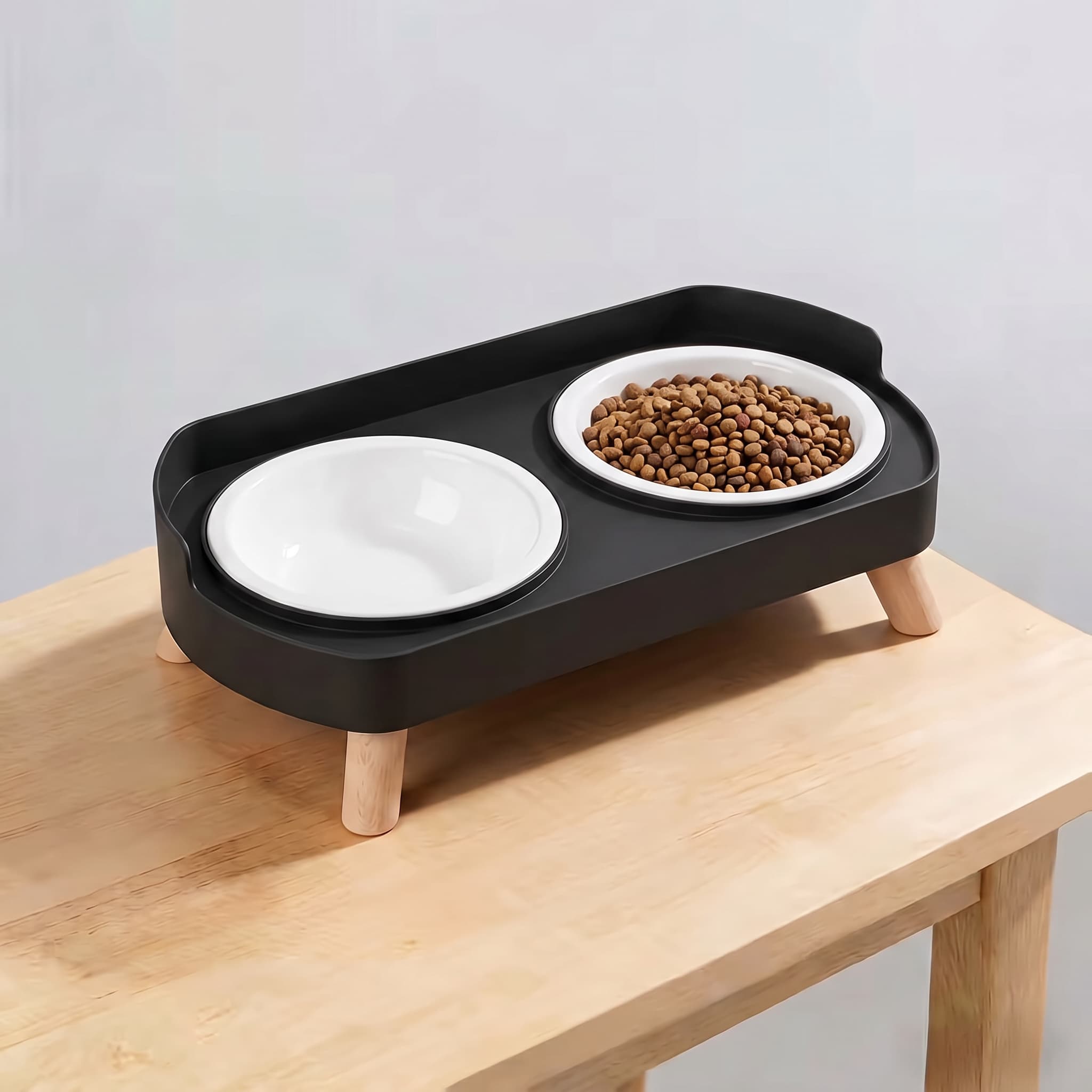Classic black elevated double pet feeding station with plain white plastic bowls and wooden legs on light wooden table