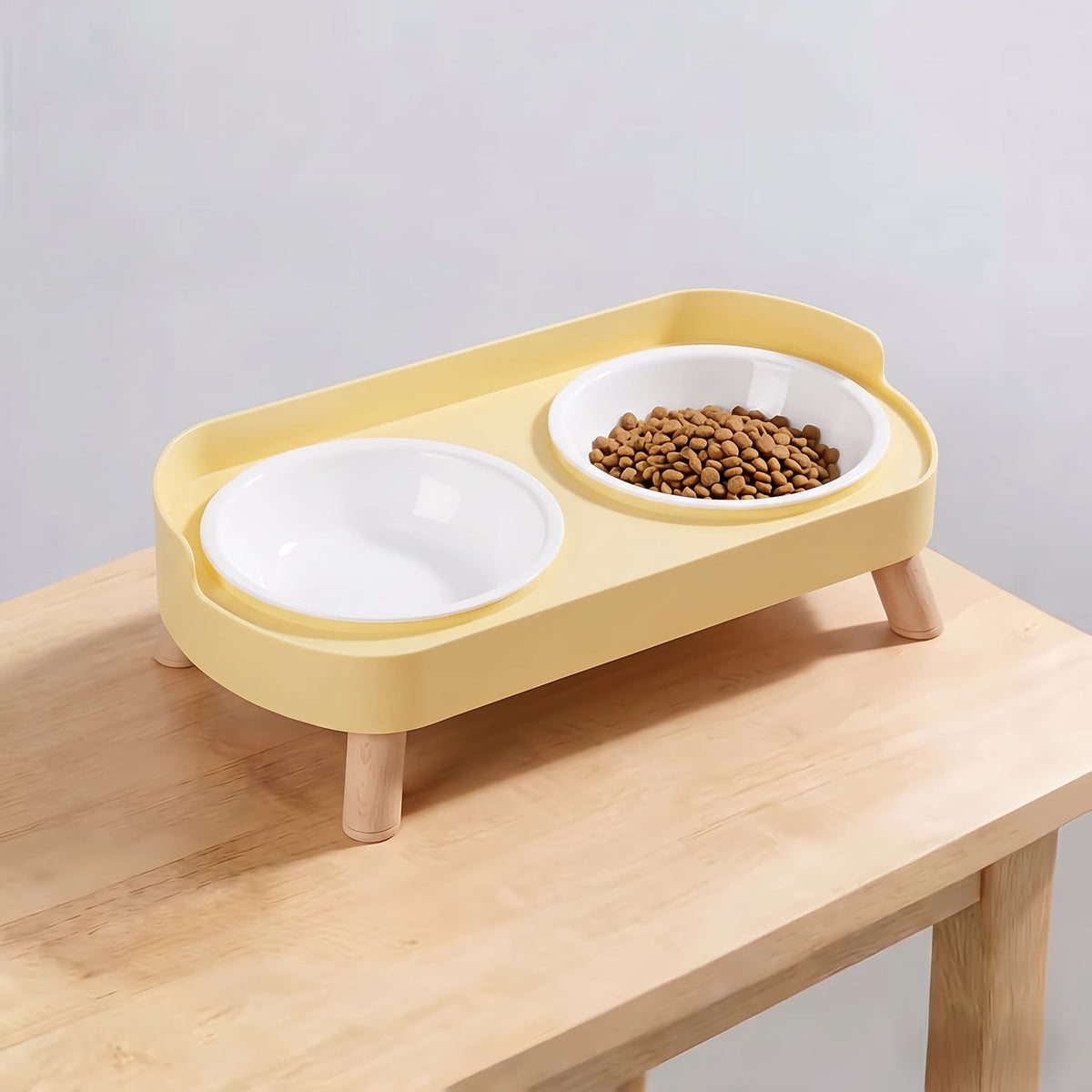 Lemon yellow elevated double pet feeding station with plain white plastic bowls and wooden legs on light wooden table