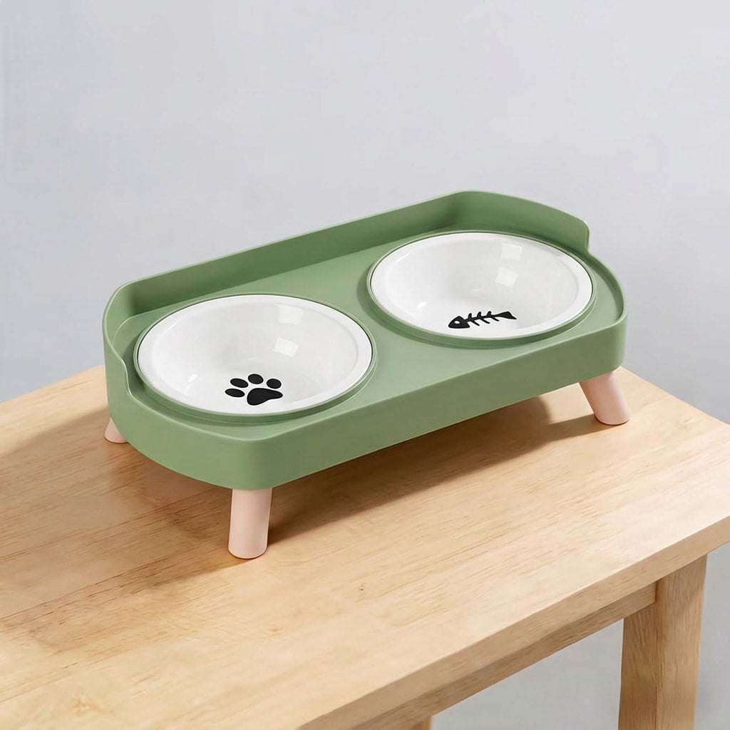 A green elevated double pet feeder with two white ceramic bowls on a light wood table against a neutral gray background.