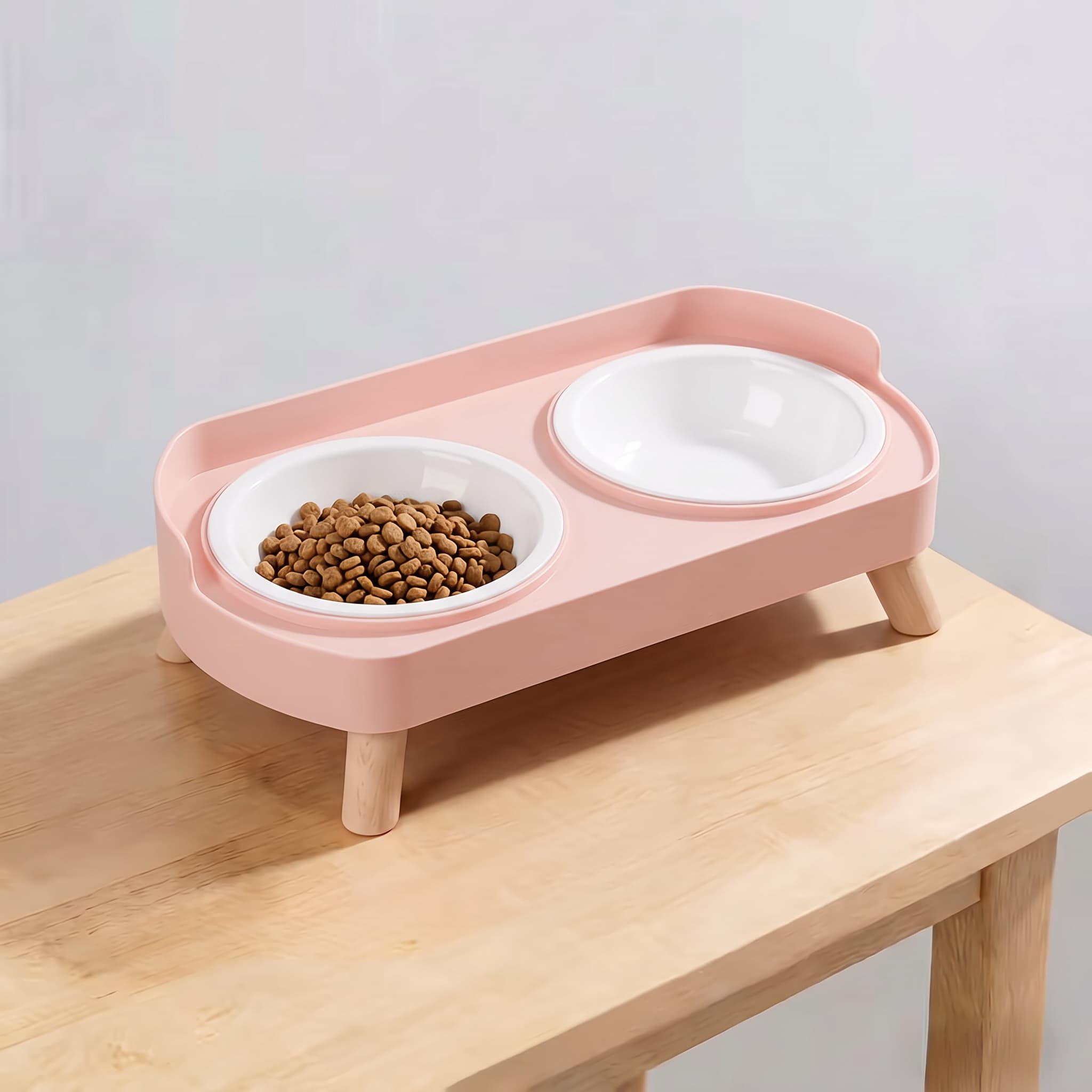 Sakura pink elevated double pet feeding station with plain white plastic bowls and wooden legs on light wooden table
