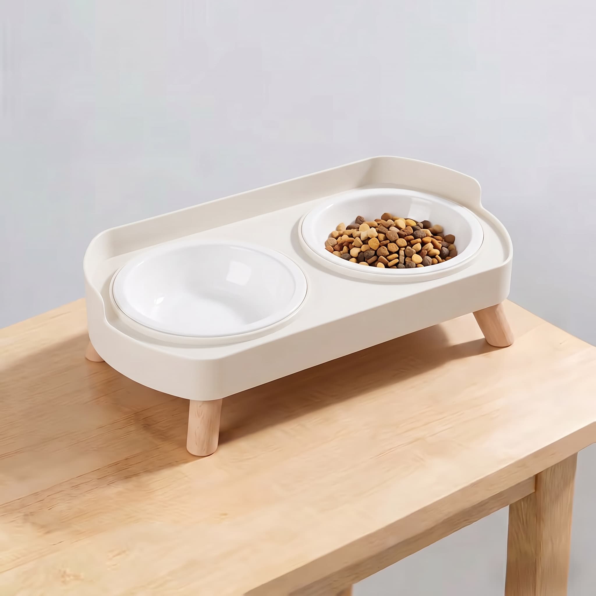Ivory white elevated double pet feeding station with plain white plastic bowls and wooden legs on light wooden table