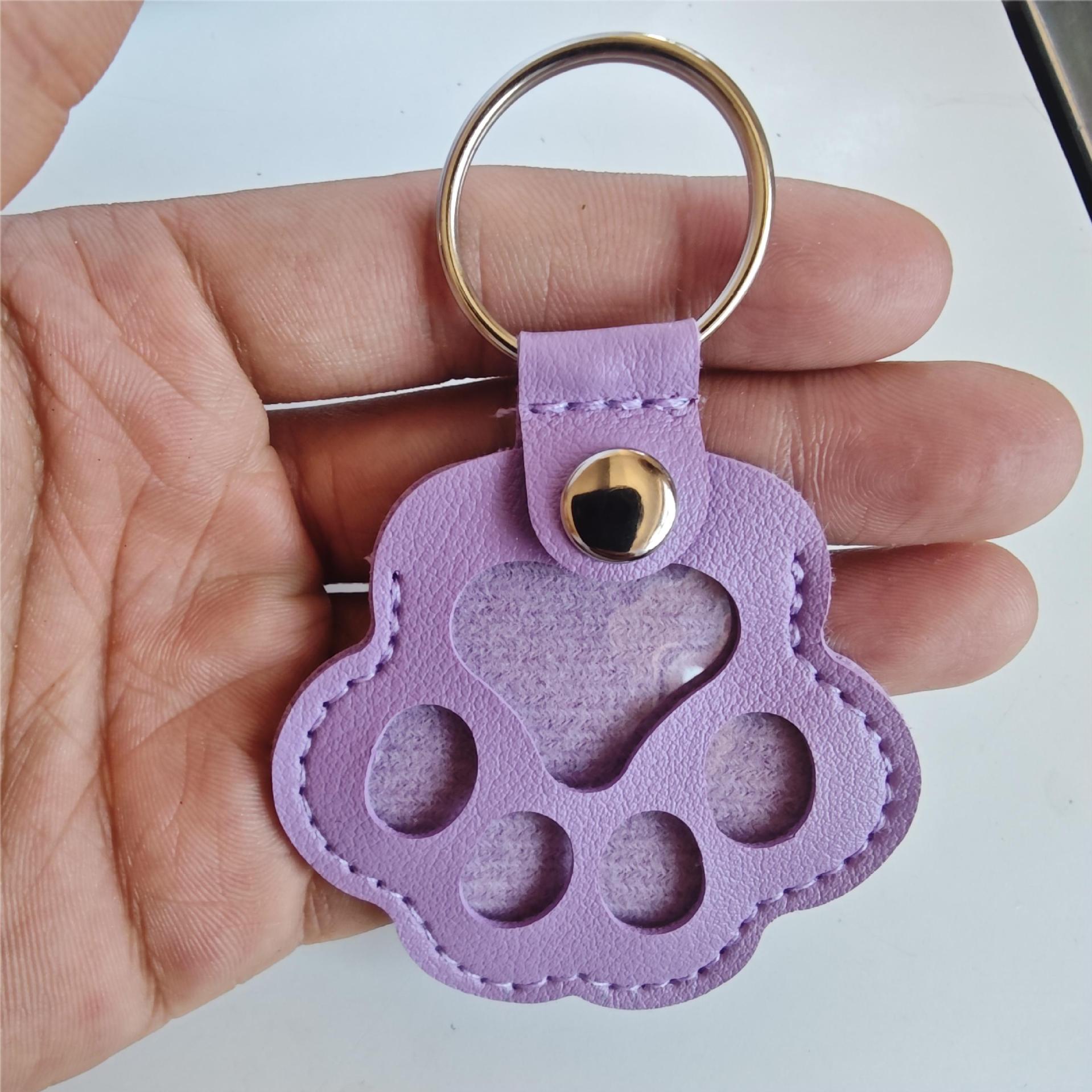 Purple paw-shaped keychain held in a hand against a white background