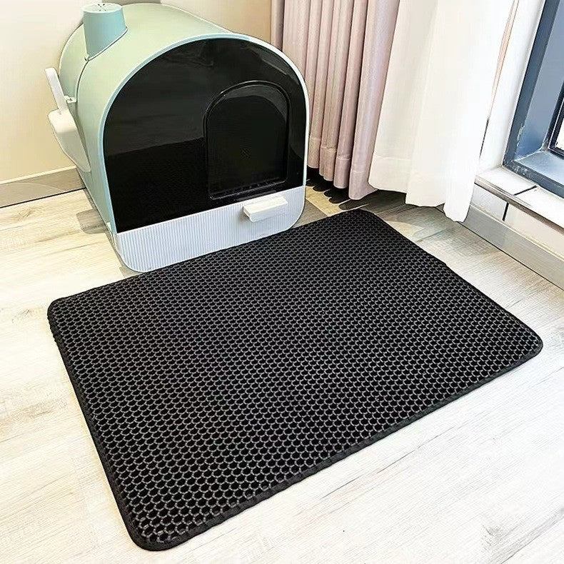 Black honeycomb litter mat in front of a cat litter box on a light wood floor.