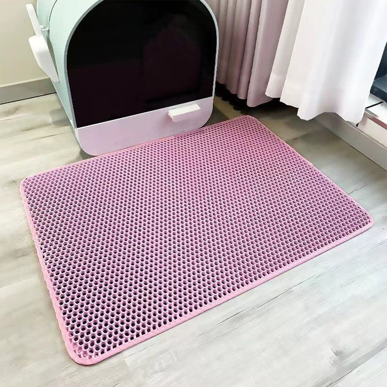 Pink litter mat with a textured pattern on a light wooden floor, next to a white pet litter box.