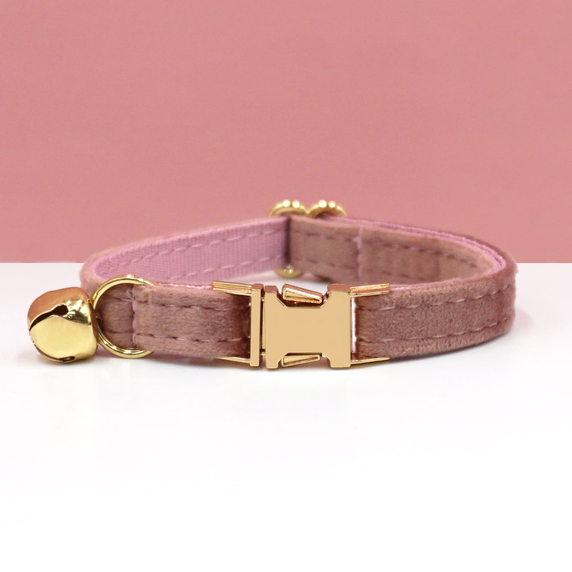 Pink cat collar with gold hardware on a white surface and pink background