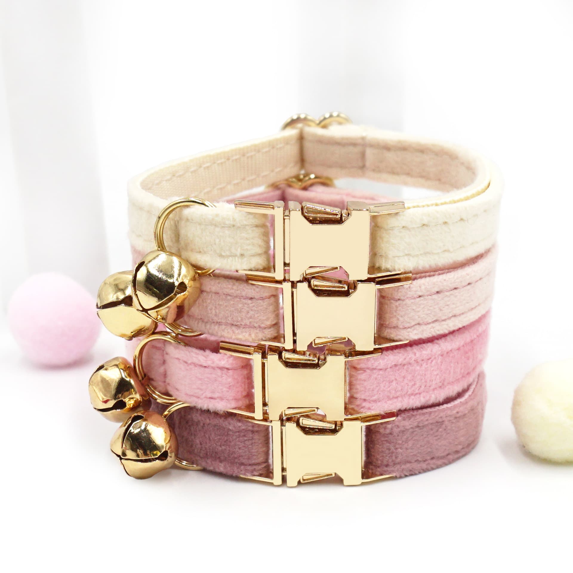 several coloured cat collars with bell with pink and gold accents on a white background