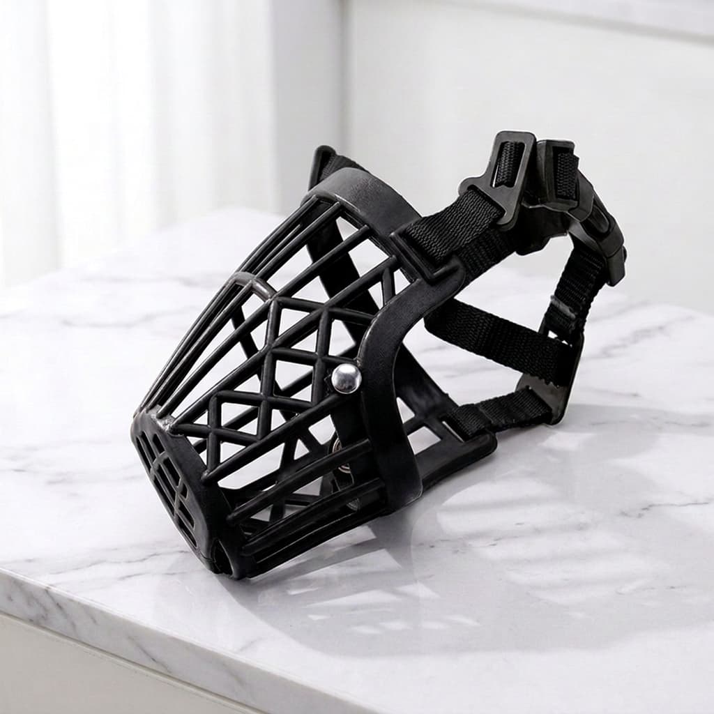 A black plastic dog muzzle with an adjustable strap and quick-release buckles, resting on a white marble surface.