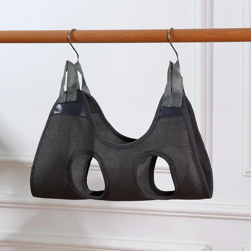 Black mesh cat harness with straps hanging on a wooden rod against a white wall.