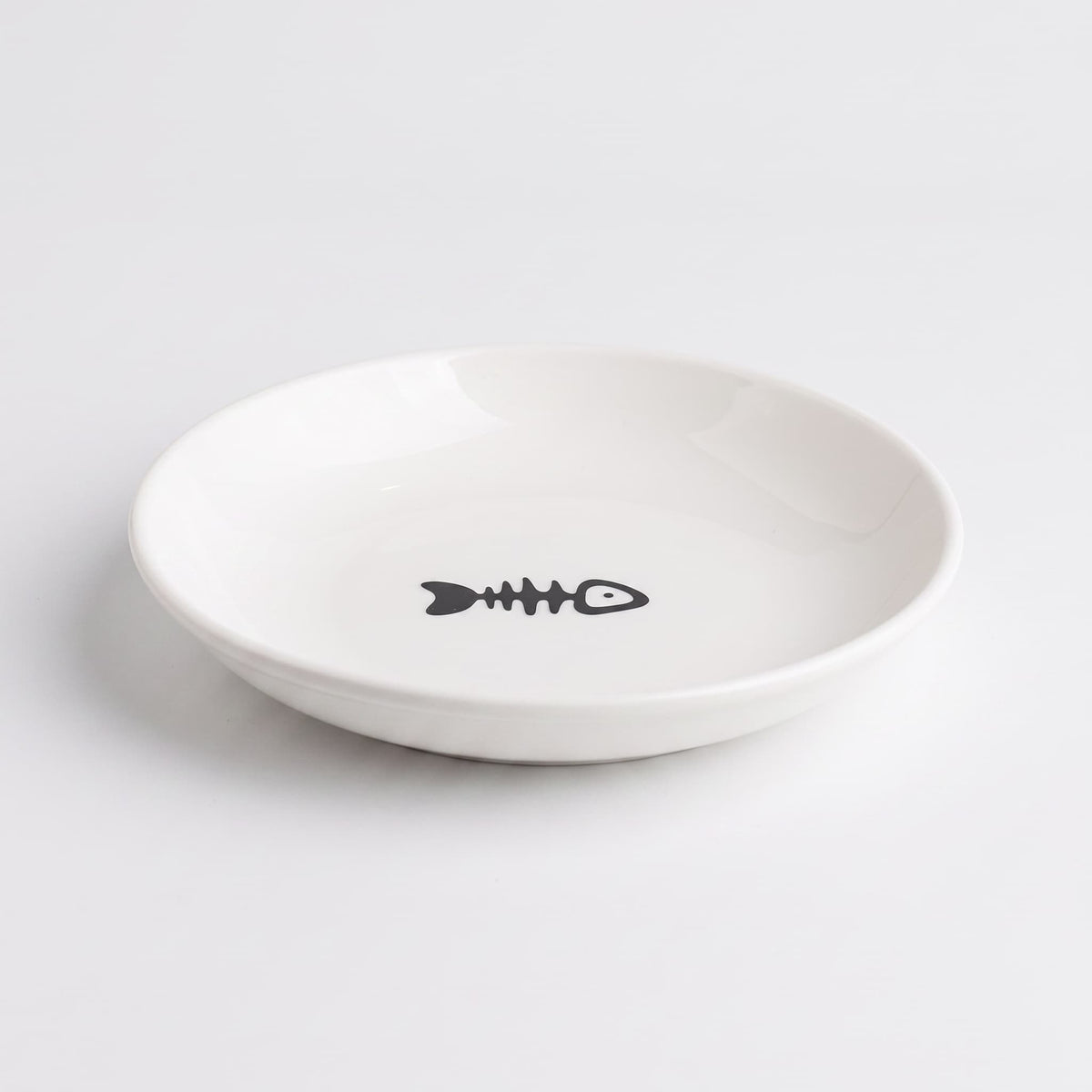 A white ceramic shallow bowl featuring a minimalist black fish skeleton graphic printed in the center, set against a clean white background.