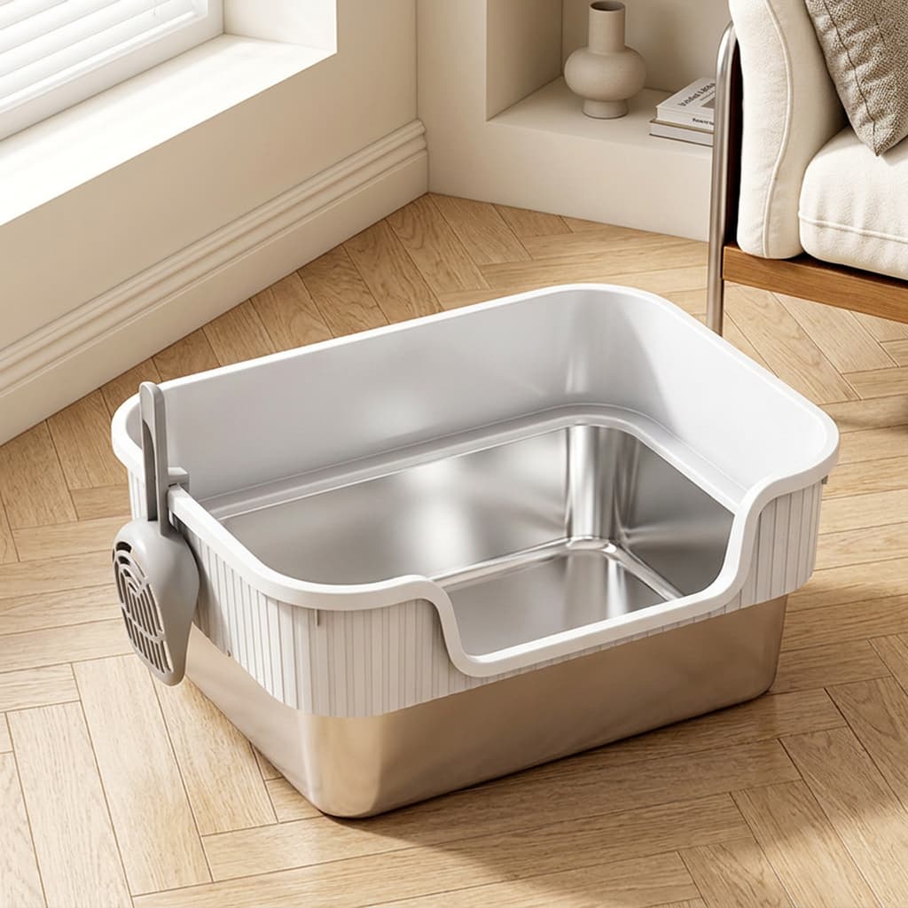 A stainless steel and white plastic litter box with a side-mounted dust collector, shown on a light wood herringbone floor in a modern living room setting.