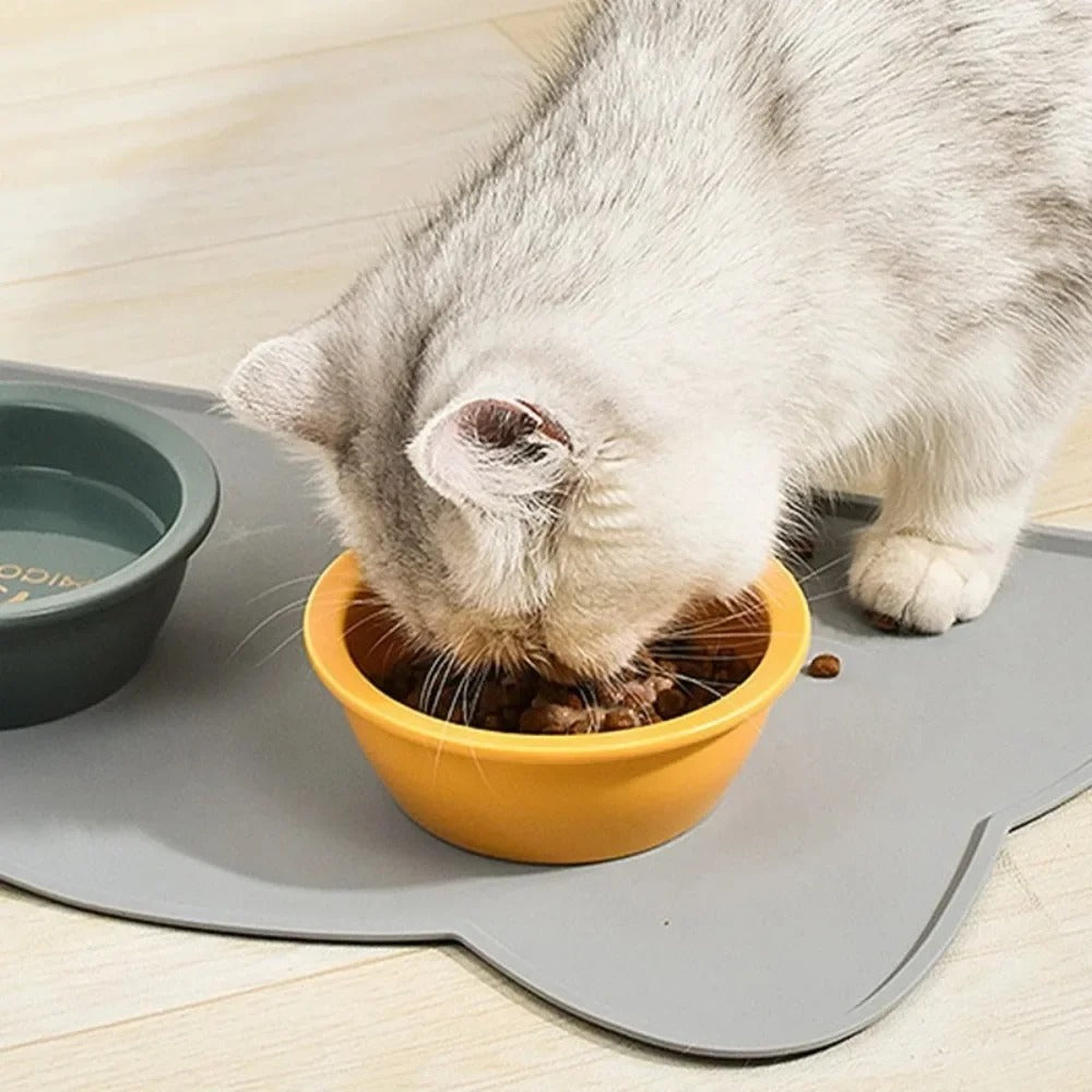 Cat eating from a yellow bowl on a grey mat with a wooden floor background