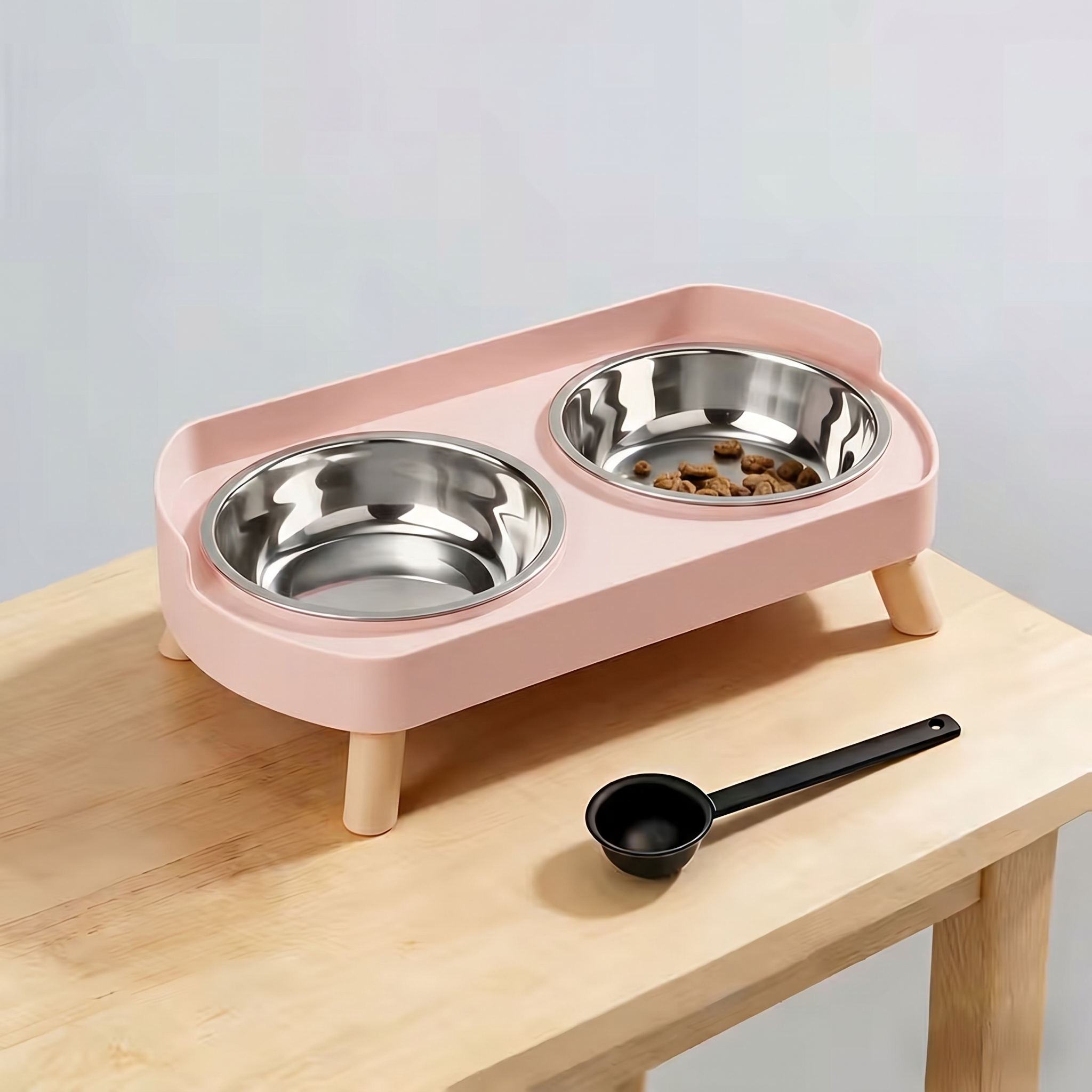 Pink pet feeder with two metal bowls on a wooden surface.