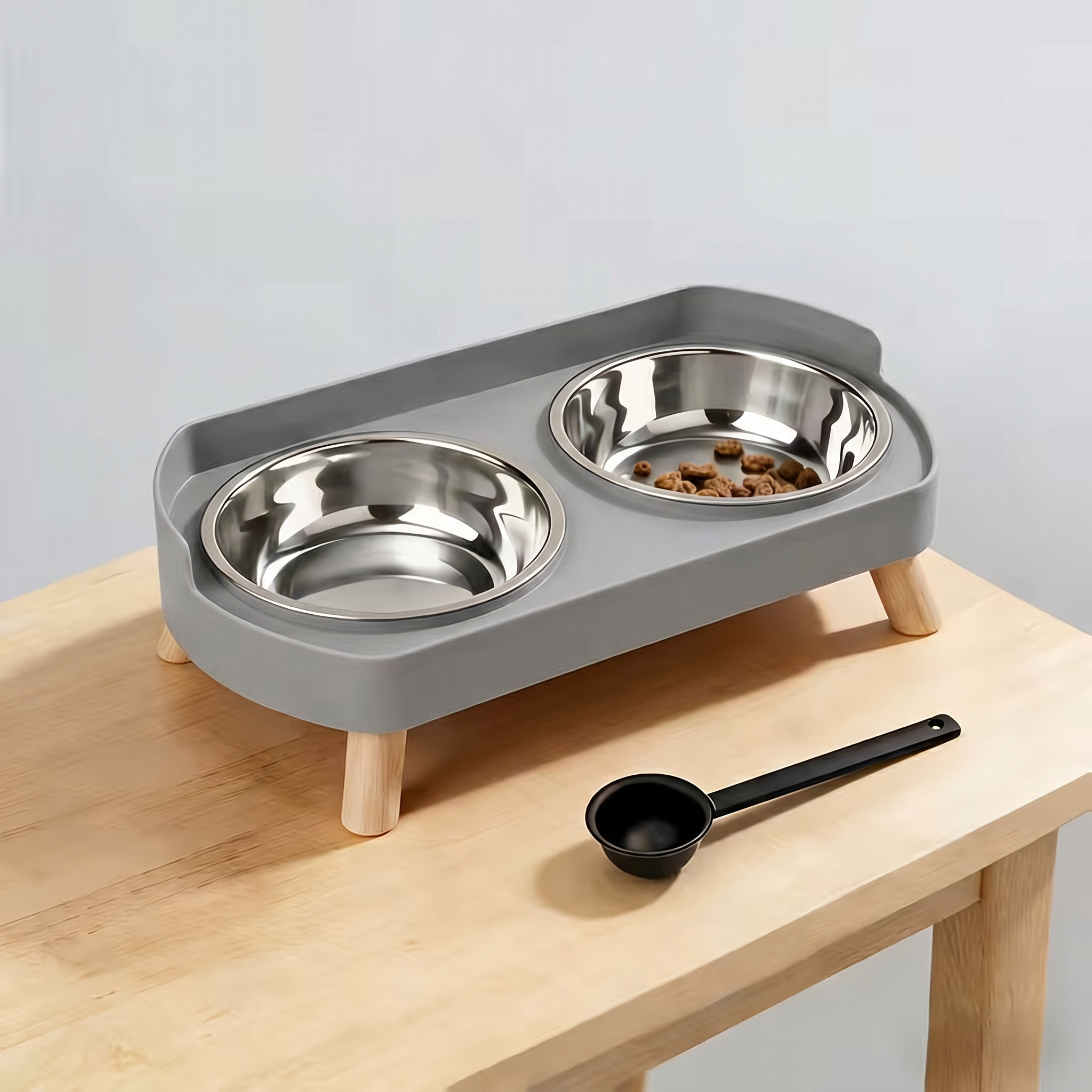 Pet feeding station with two stainless steel bowls on a gray stand, placed on a wooden surface.