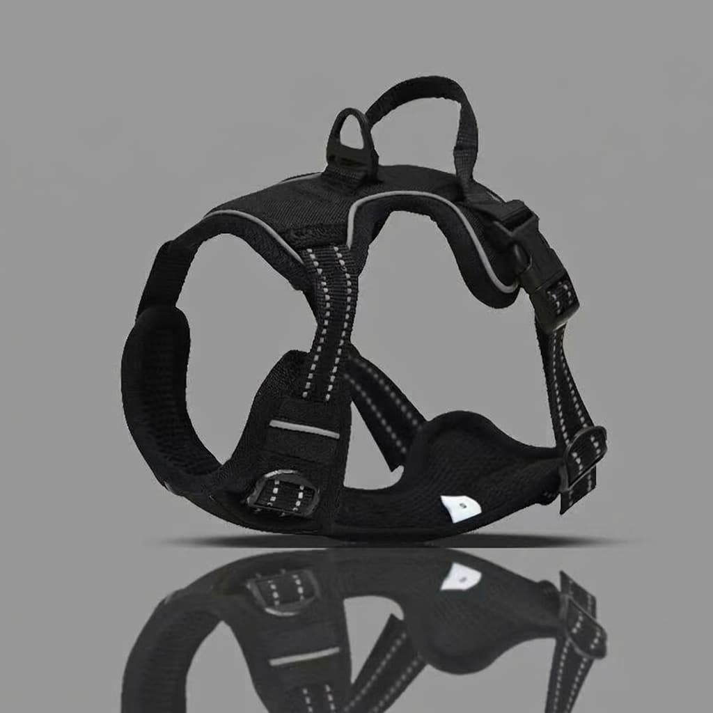 A black dog harness with reflective white stitching and a small white reflective patch, displayed on a solid gray background with a reflection below.