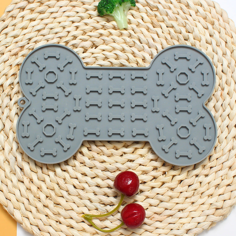 Grey bone-shaped mat on a woven surface with red berries and green leaves.