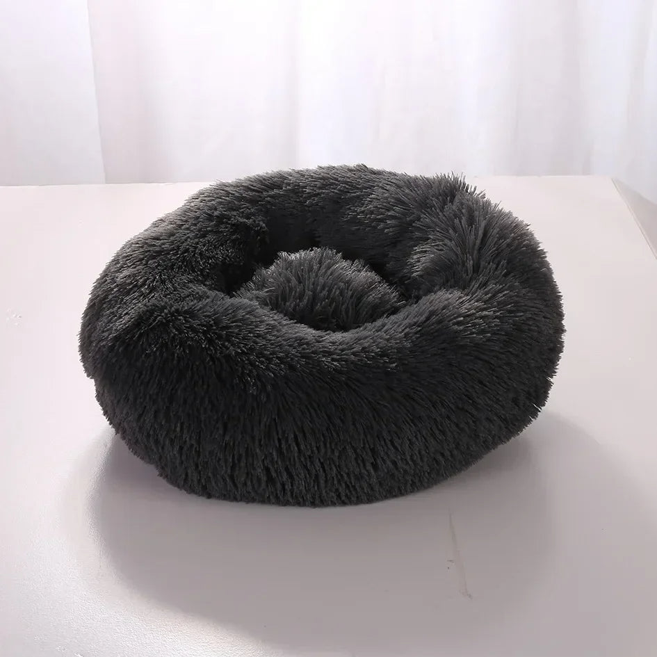 Fluffy dark grey pet bed on a white surface with a white curtain background