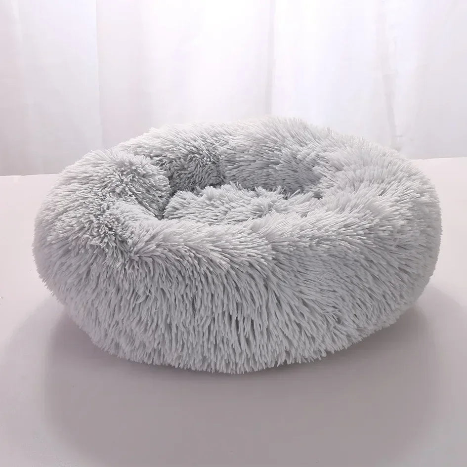 Fluffy grey pet bed on a white surface with a light gray curtain background