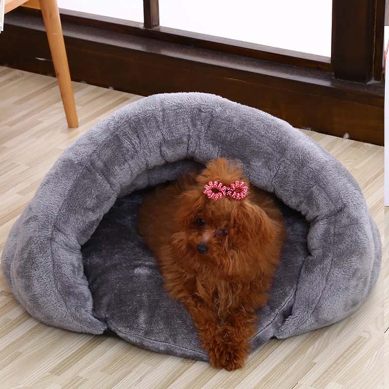 Small dog with a pink bow inside a grey pet bed on a wooden floor.