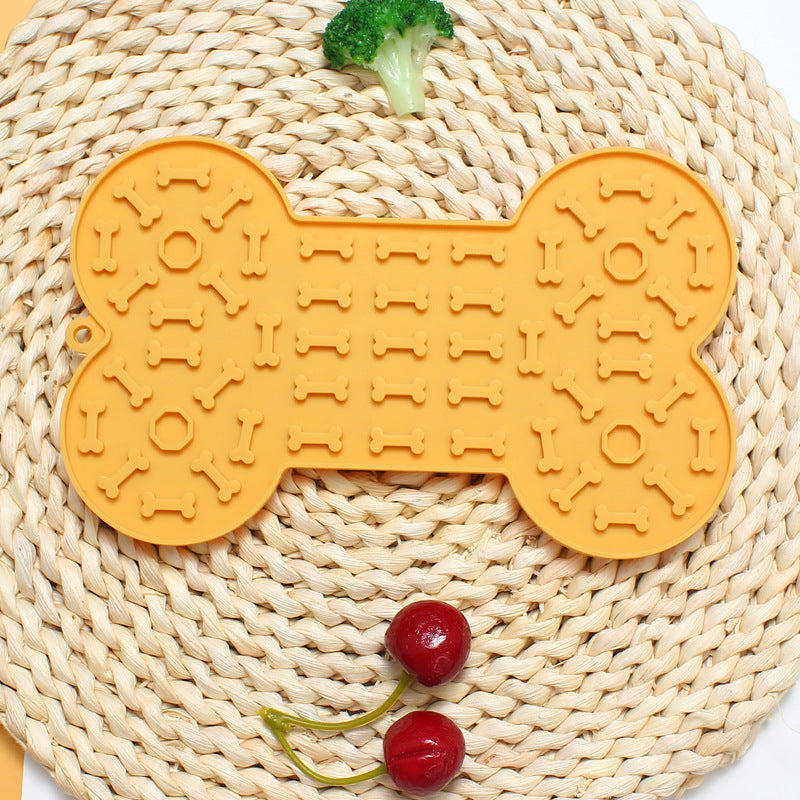 Yellow bone-shaped mat on a woven surface with broccoli and cherries.
