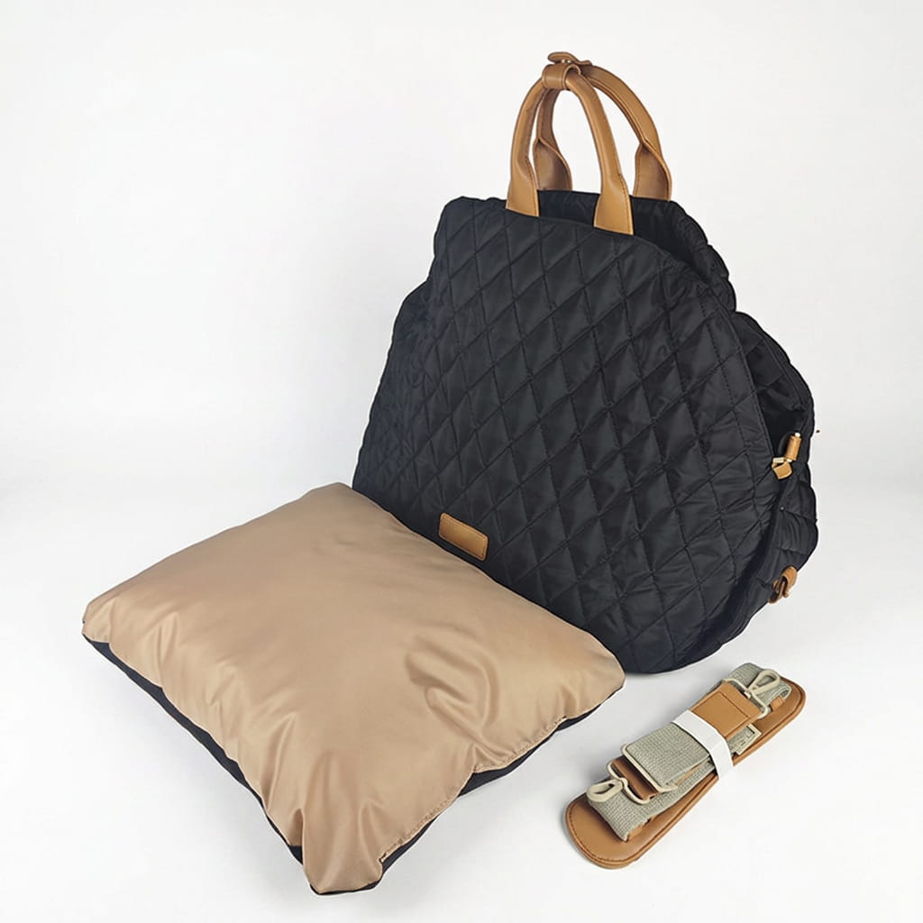 A black quilted handbag bag with tan leather handles and a matching beige insert pillow, shown on a clean white background with a shoulder strap beside it.
