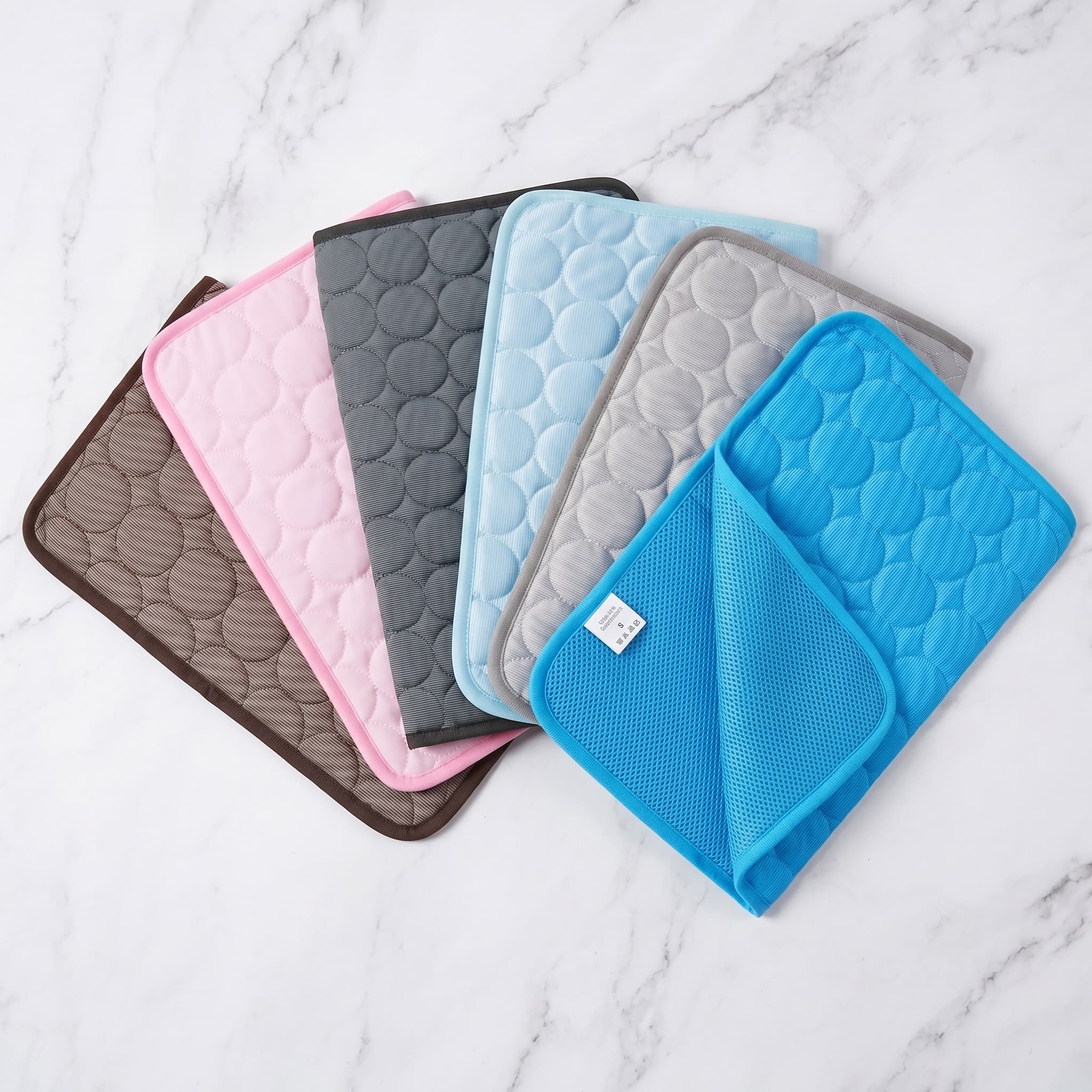 Set of six quilted pet cooling mats in different colours on a marble surface