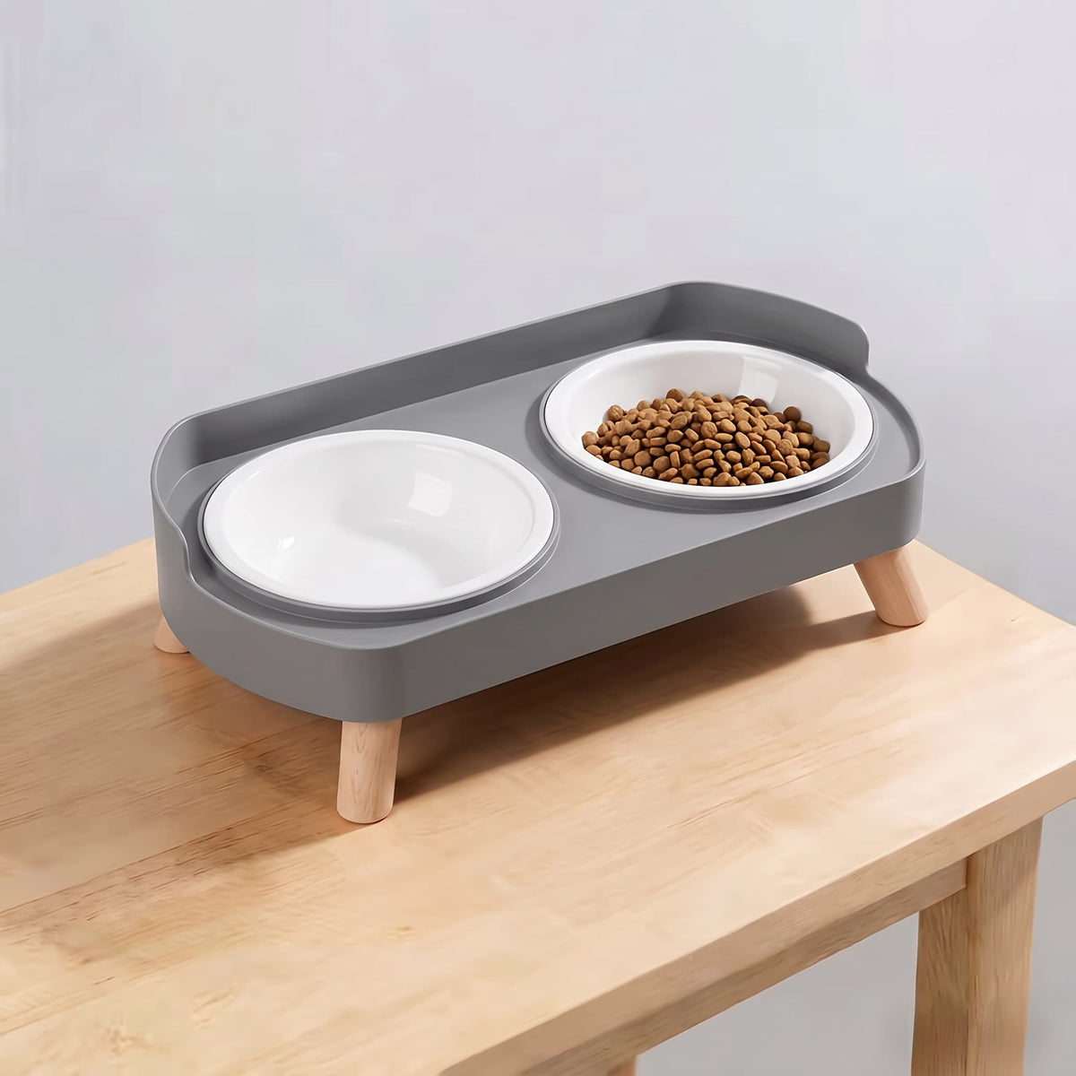 Minimalist grey elevated double pet feeding station with plain white plastic bowls and wooden legs on light wooden table