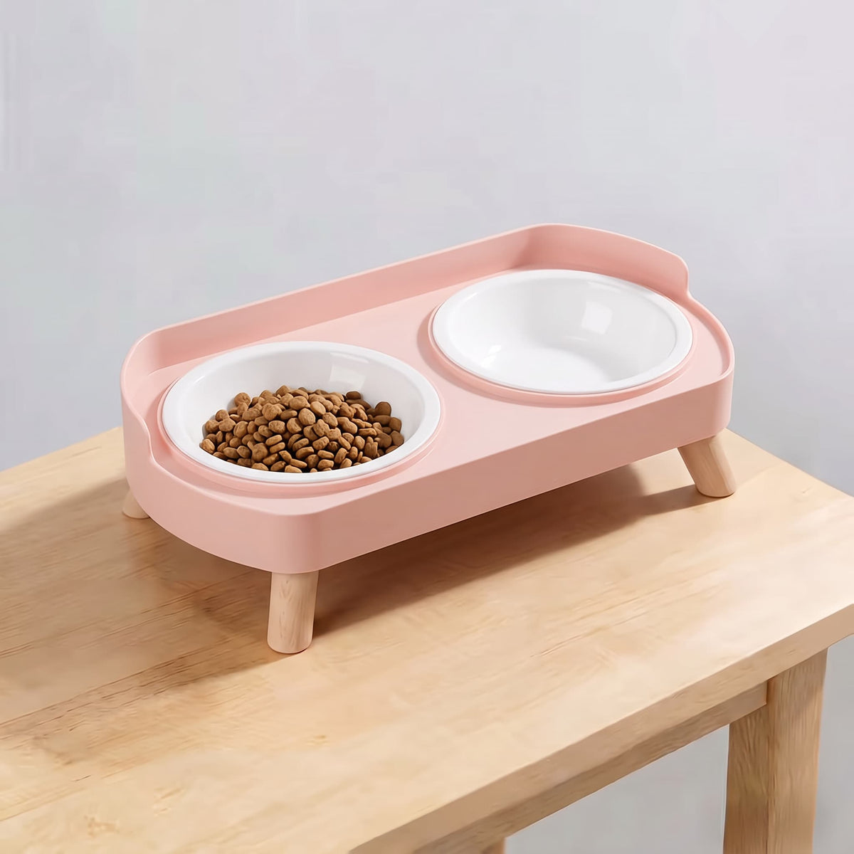 Sakura pink elevated double pet feeding station with plain white plastic bowls and wooden legs on light wooden table