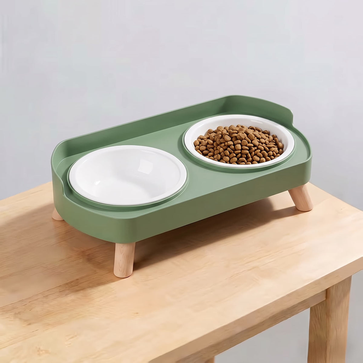Avocado green elevated double pet feeding station with plain white plastic bowls and wooden legs on light wooden table