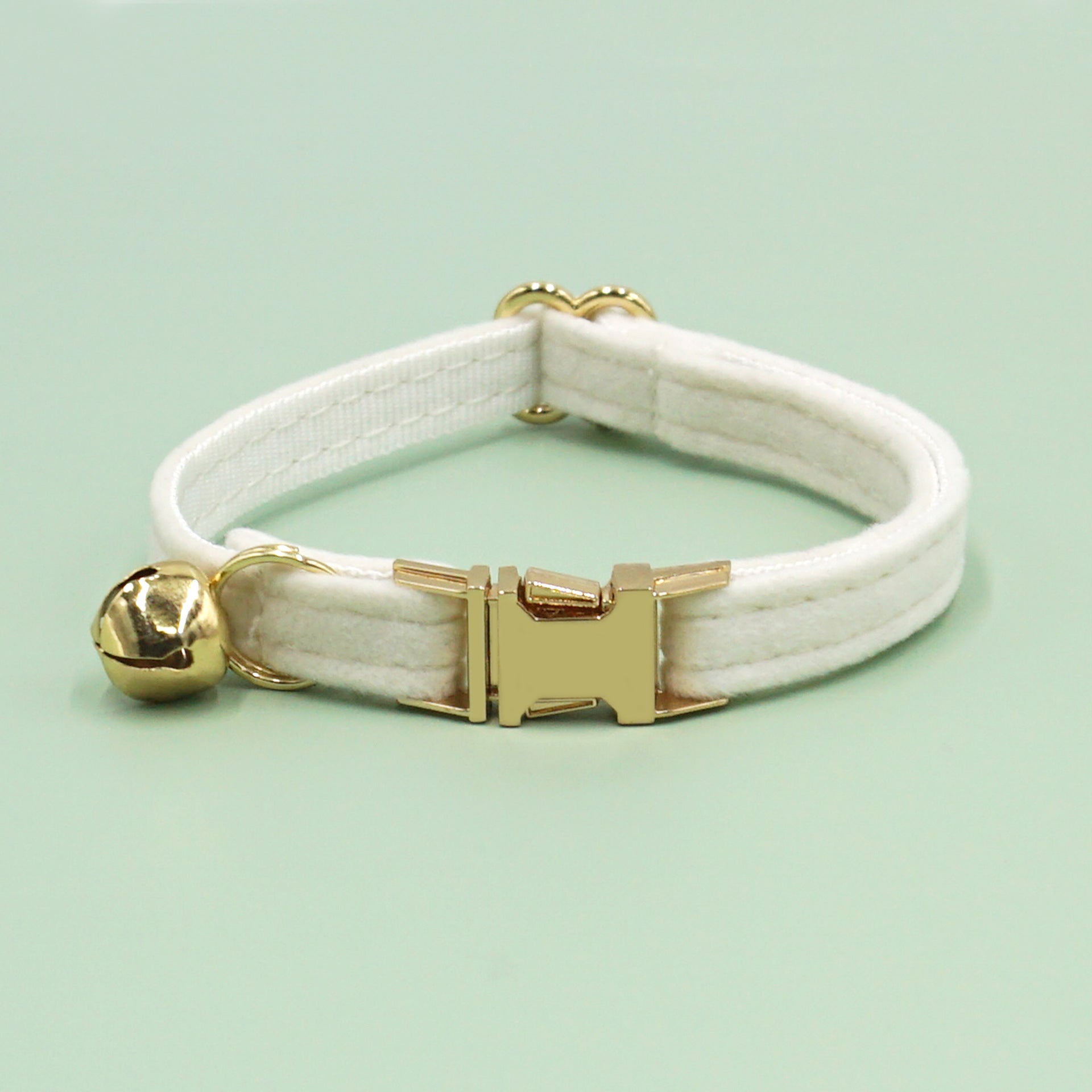 White velvet cat collar with gold clasp and bell on a light green background