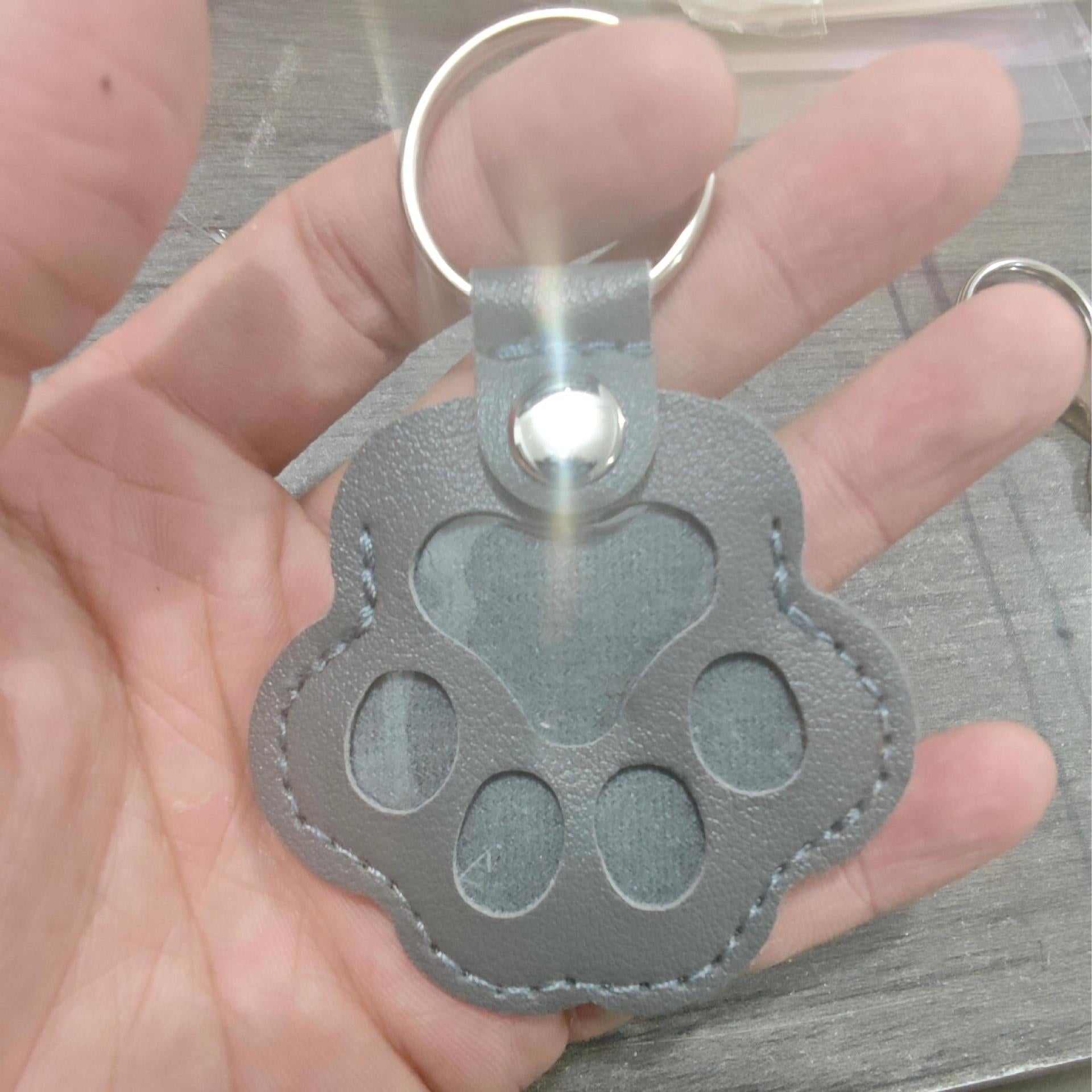 Gray paw-shaped keychain held in a hand on a wooden surface