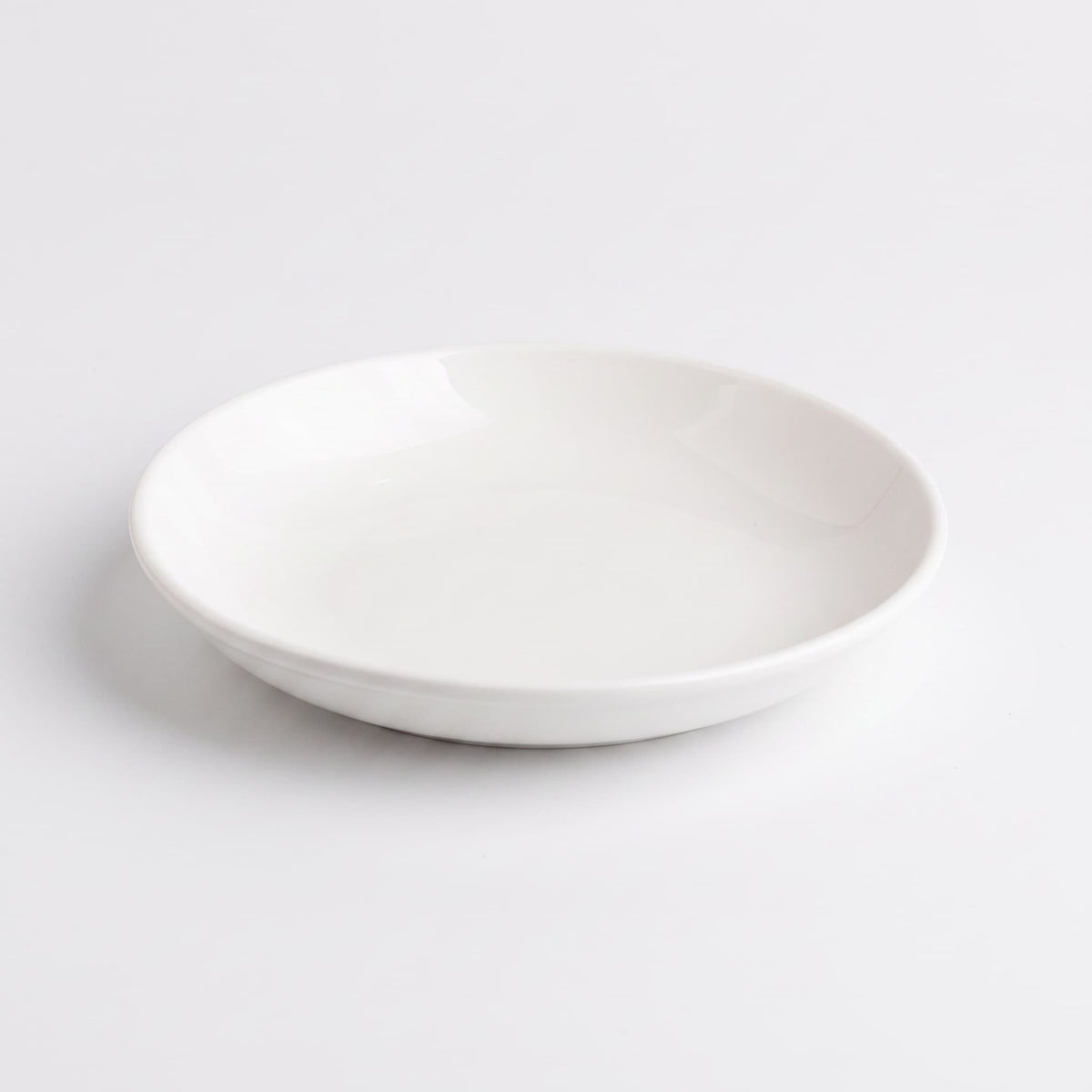 A minimalist white ceramic shallow bowl/plate with a smooth, glossy finish, photographed from a direct overhead angle on a seamless white background.