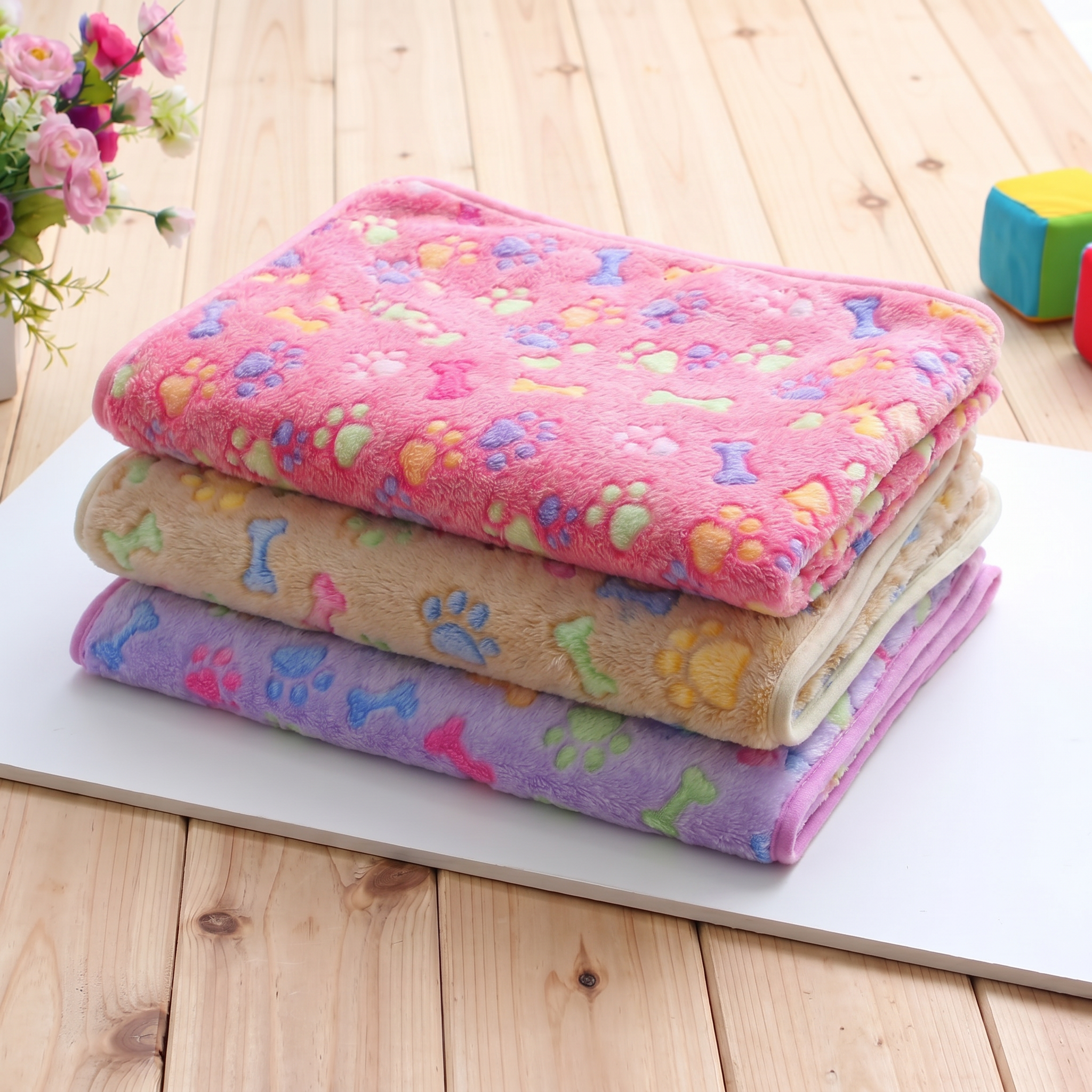 Stack of colorful pet blankets with paw and bone patterns on a wooden floor.
