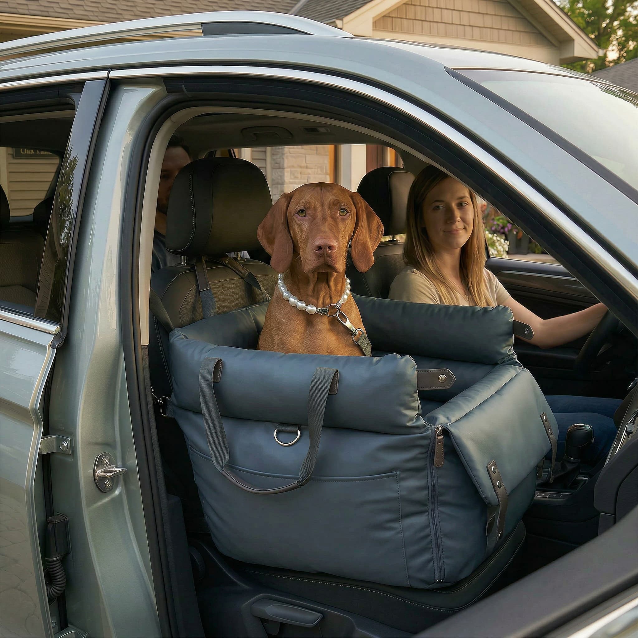 Dog in a car seat carrier with a woman driving and a man in the passenger seat.