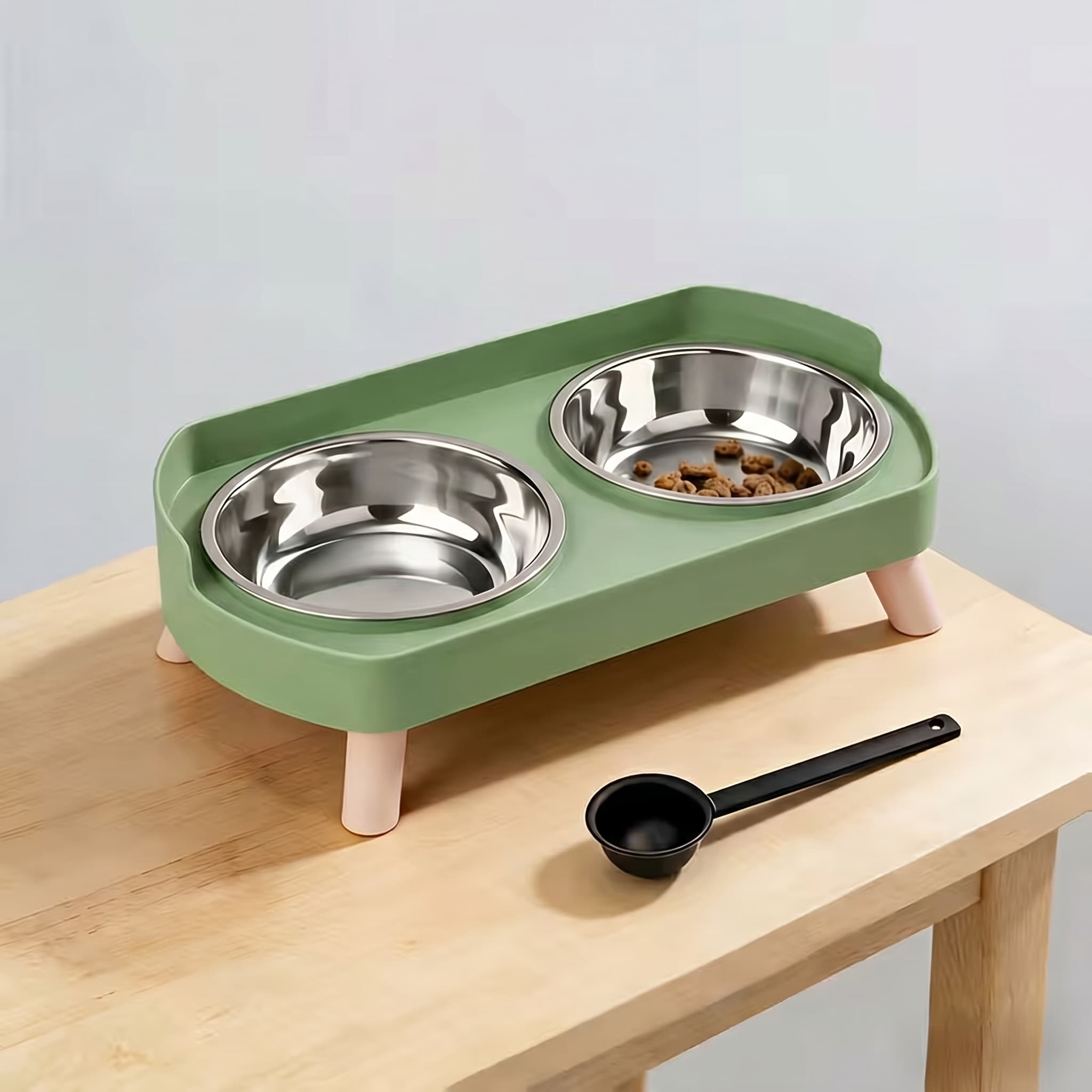Green elevated pet feeder with two metal bowls on a wooden surface.