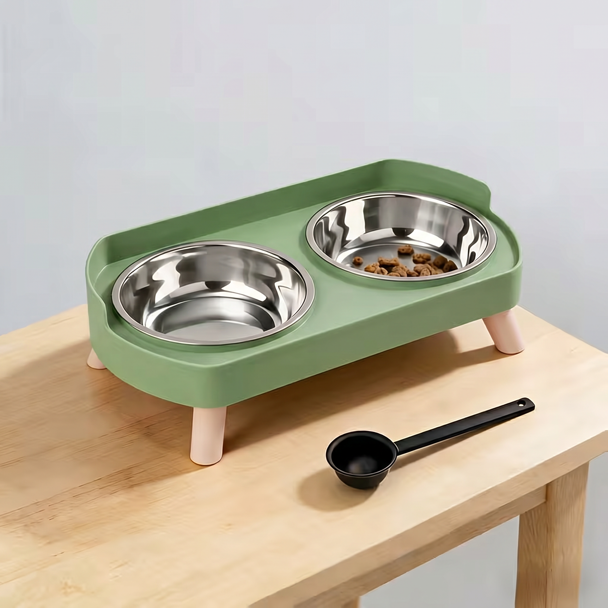Green elevated pet feeder with two metal bowls on a wooden surface.