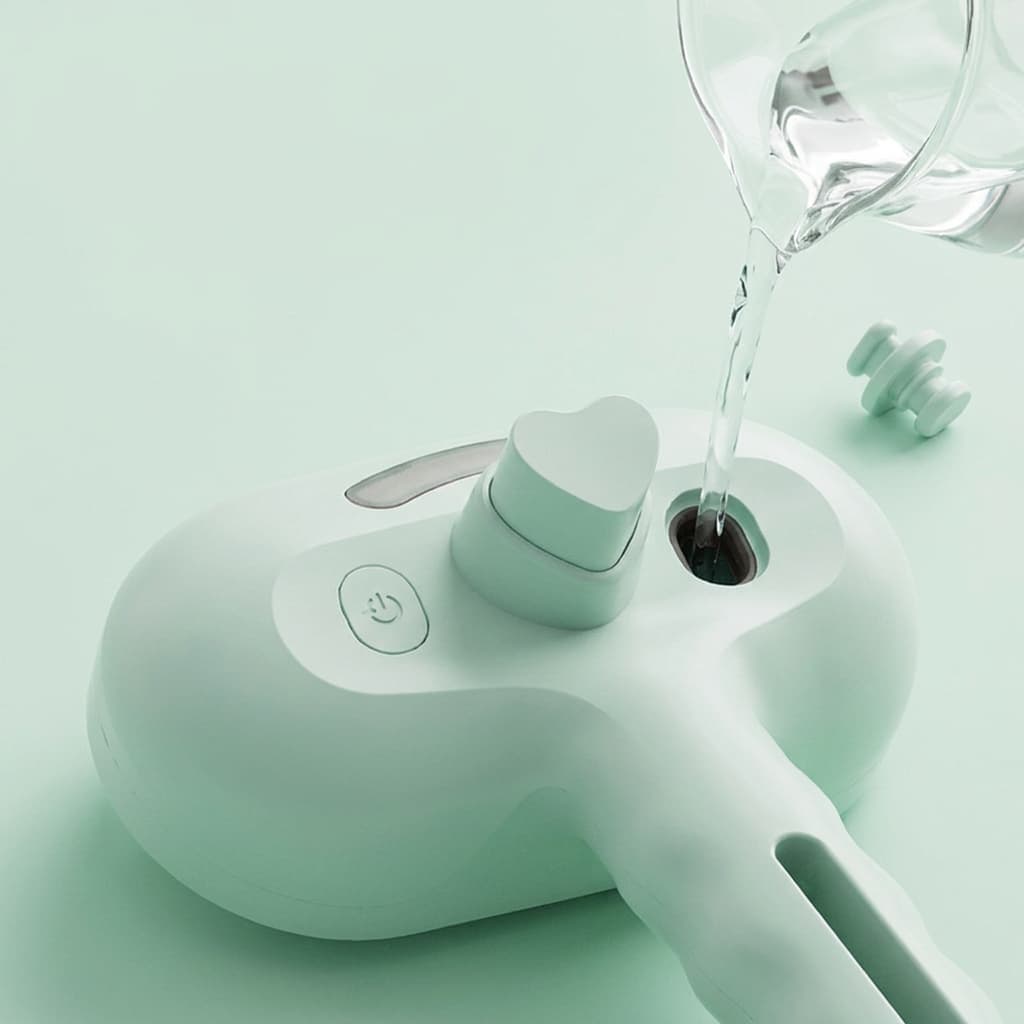 Close up of mint green electric steam spray pet grooming brush showing water filling port and heart shaped self clean button
