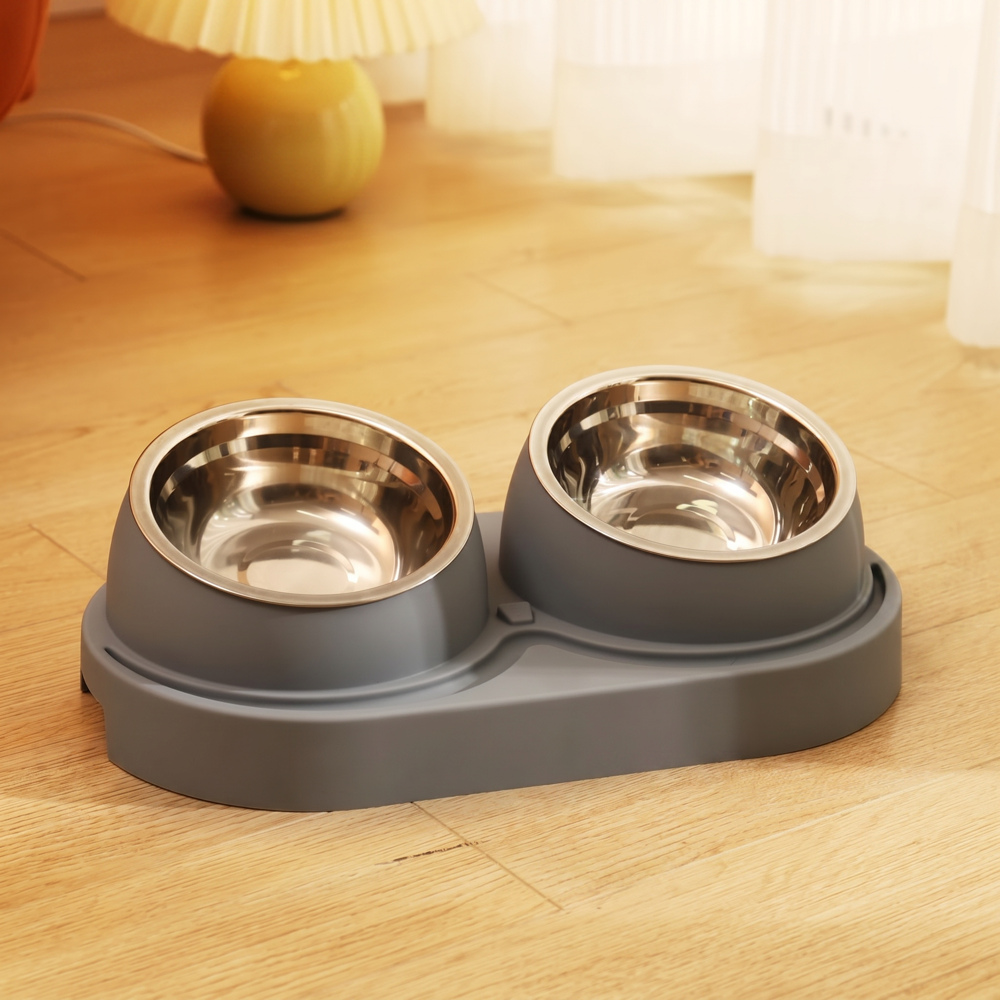 Grey pet feeder with two stainless steel bowls on a wooden floor.